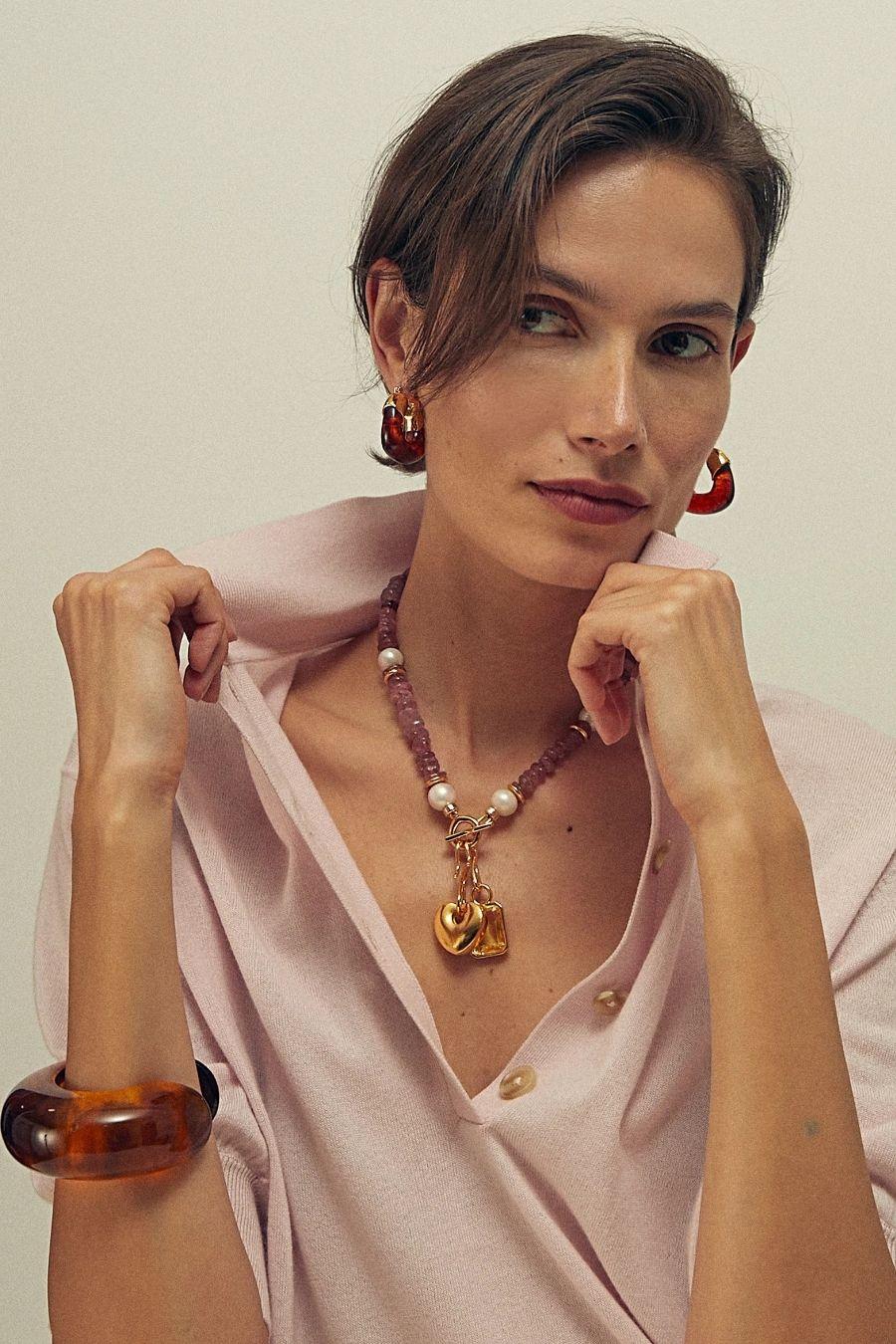Model in blush top wearing statement pendant necklace, tortoiseshell cuff, red drop earrings