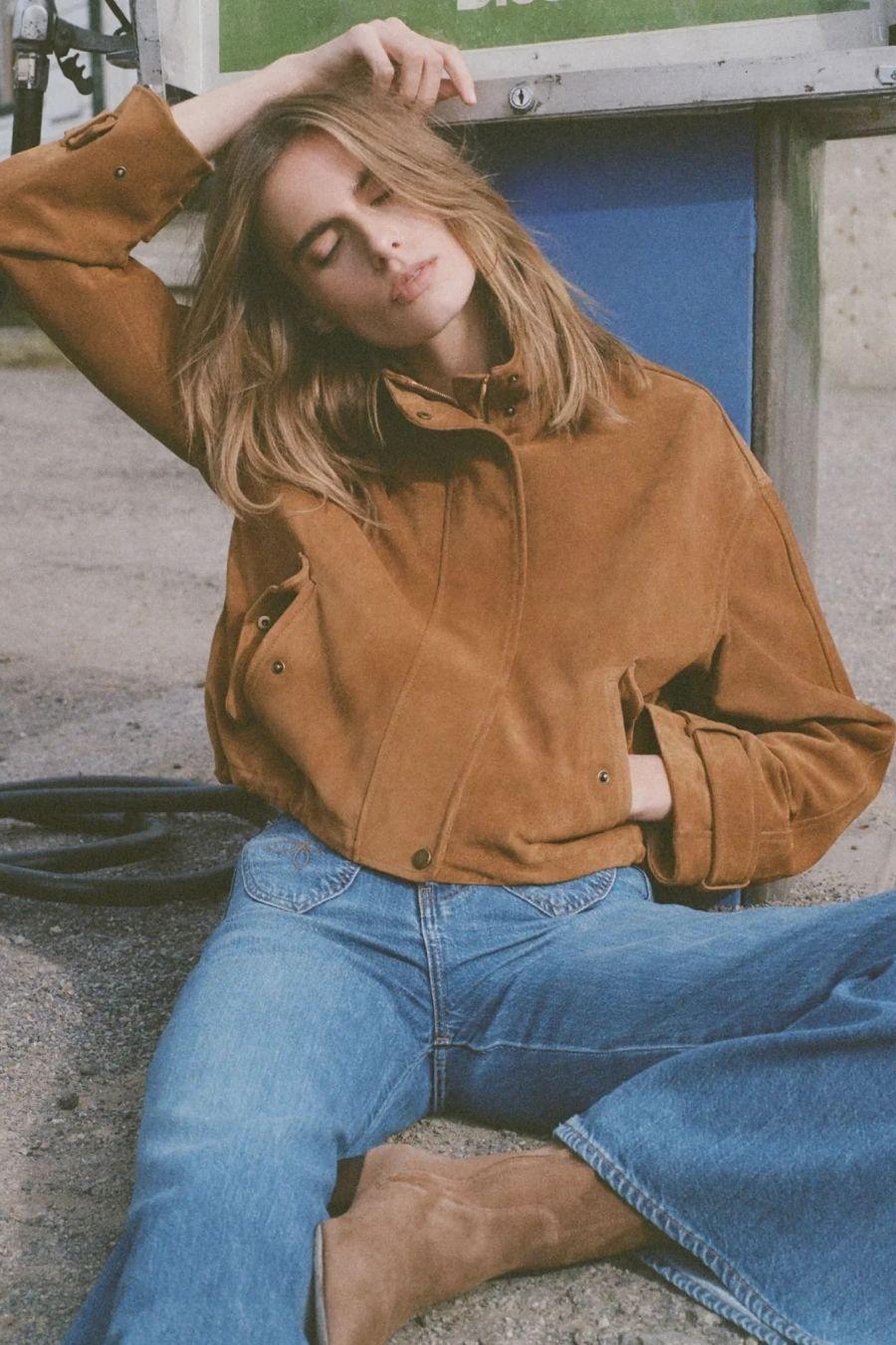 Model in denim jeans and tan boots, seated outdoors