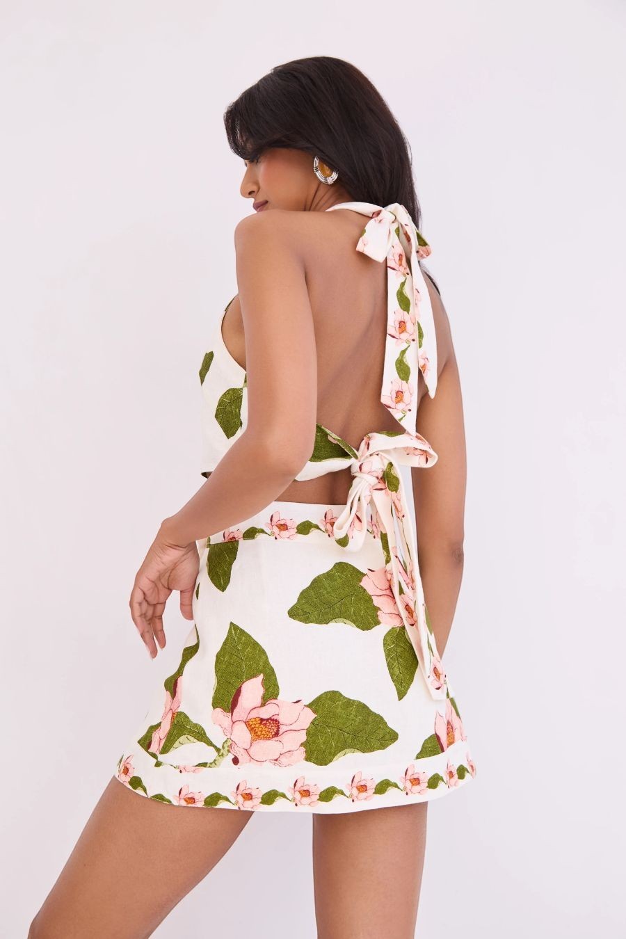 Bunny and Babe Winnetka Fischer mini wrap skirt in ivory linen with lotus print, green leaves, pink flowers, and decorative raffia trim.